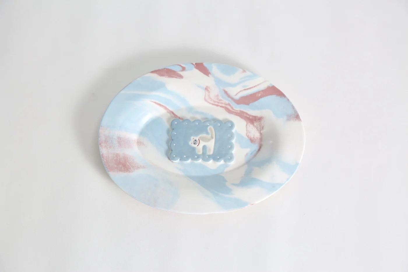 Blue, pink and white ceramic plate with a raised cat motif