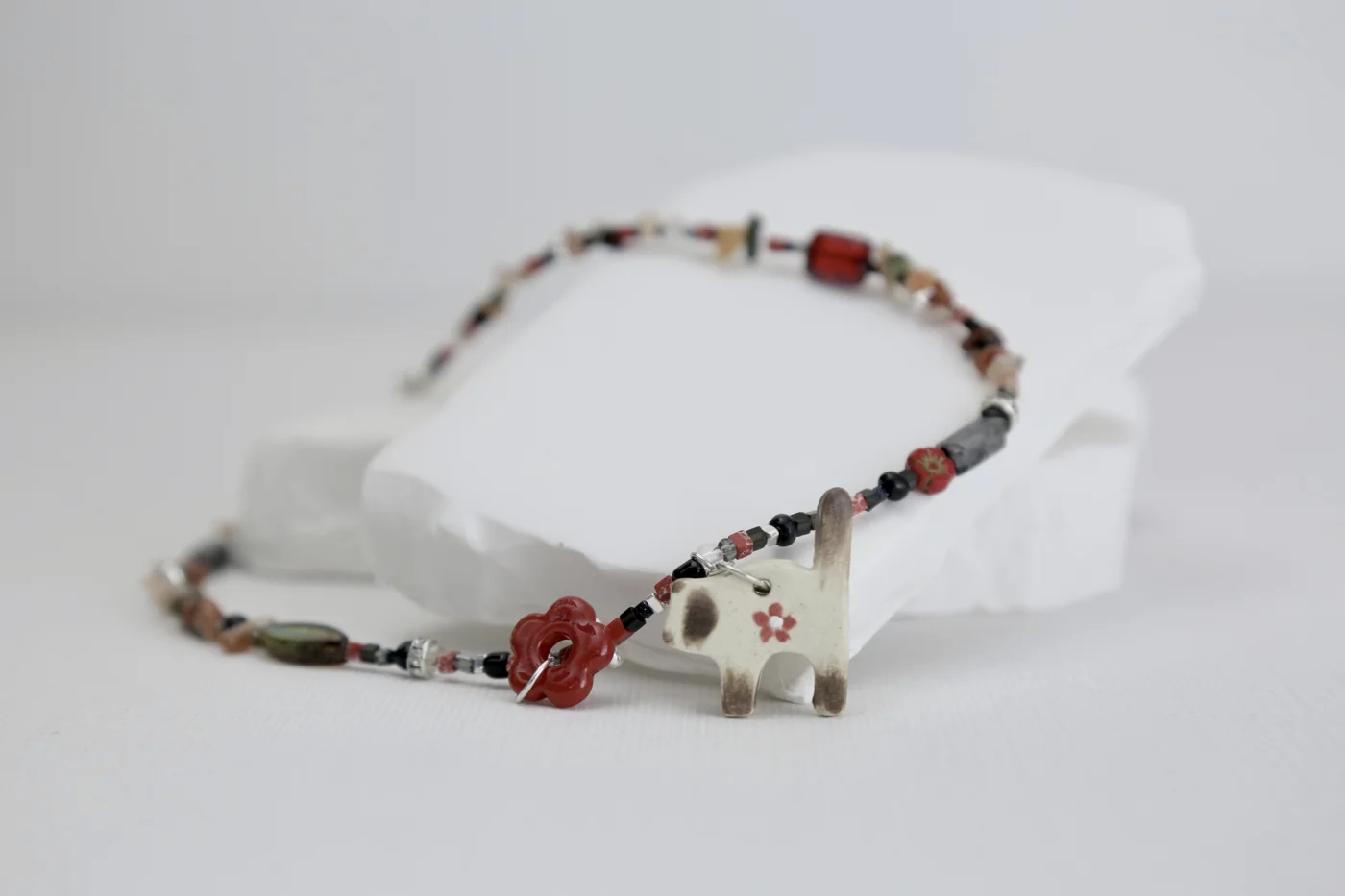 A small cat-themed ceramic pendant on a beaded cord
